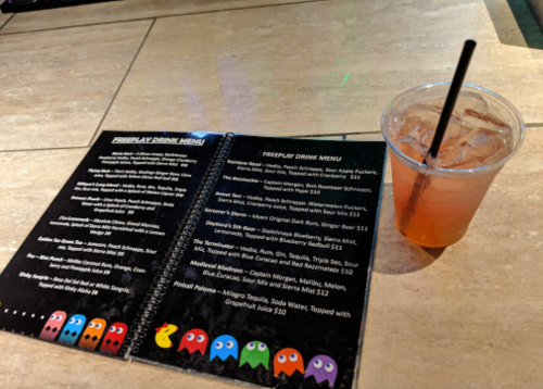 A drink menu featuring various beverages next to a cup of a colorful drink with a straw on a table.
