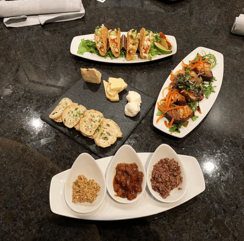 A variety of dishes including tacos, salads, cheese, and spreads served on elegant white plates.