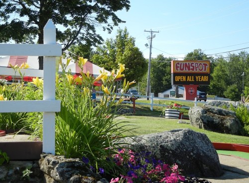 A colorful mini-golf course with flowers in the foreground and a sign for Funspot, open all year, in the background.