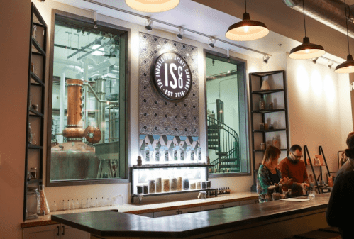 A modern bar with a distillery backdrop, featuring bottles and a decorative logo on the wall.