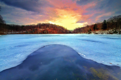 A serene frozen lake at sunset, with vibrant colors reflecting on the ice and trees in the background.