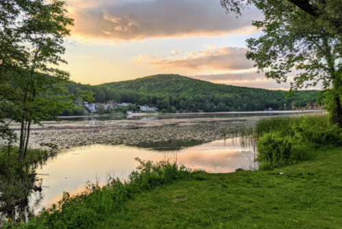 A serene lake at sunset, surrounded by lush greenery and hills, reflecting soft colors in the water.