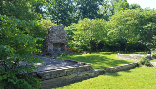 Ruins of a stone structure surrounded by lush greenery and trees in a serene outdoor setting.