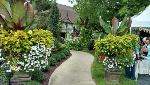 A scenic garden path lined with vibrant flower pots and lush greenery, leading to a charming gazebo.