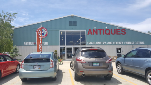 Exterior of an antique store with a large sign, featuring parked cars in front and a clear blue sky.