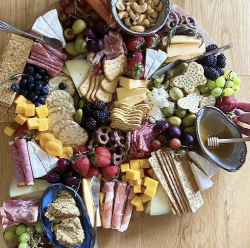 A colorful charcuterie board featuring various cheeses, meats, fruits, nuts, and crackers arranged artfully.