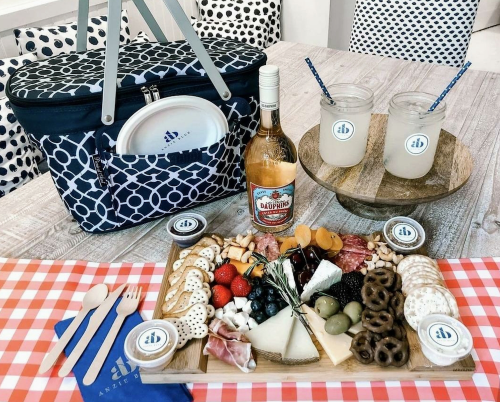 A picnic setup featuring a cooler, wine, drinks, and a charcuterie board with various cheeses, meats, and snacks.