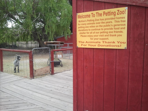 Sign welcoming visitors to a petting zoo, with a goat visible in the background and a message about donations.