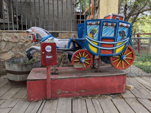 A vintage horse-drawn carriage ride-on toy, painted in bright colors, with a coin slot for 25 cents.