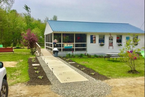 A small white building with a blue roof, surrounded by greenery and a gravel path leading to the entrance.