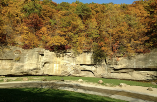 A scenic view of a rocky cliff surrounded by vibrant autumn foliage and a calm riverbank.