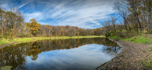 A serene river scene with autumn trees reflecting in the water under a blue sky with wispy clouds.