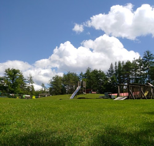 A sunny park scene with green grass, playground equipment, and fluffy clouds in a blue sky.