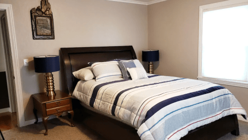 Cozy bedroom featuring a large bed with striped bedding, two bedside lamps, and a window with natural light.