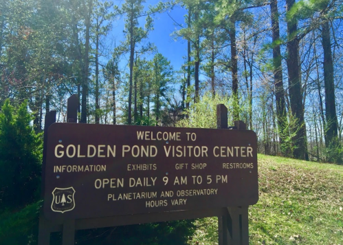 Sign for Golden Pond Visitor Center, surrounded by trees, with information about hours and facilities.