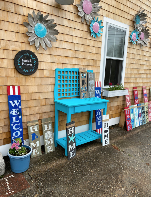 A bright turquoise table with a trellis back, surrounded by colorful wooden signs that say "Welcome" and "Home."