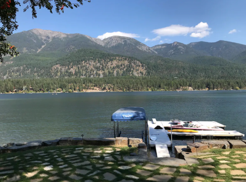 Scenic view of a lake surrounded by mountains, with a dock and boats on the water under a clear blue sky.