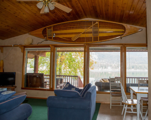 Cozy living room with a canoe on the wall, large windows overlooking a lake, and comfortable seating.