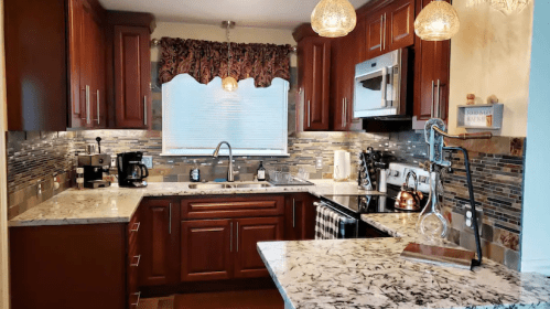 Modern kitchen with dark wood cabinets, granite countertops, and stainless steel appliances, featuring a stylish backsplash.