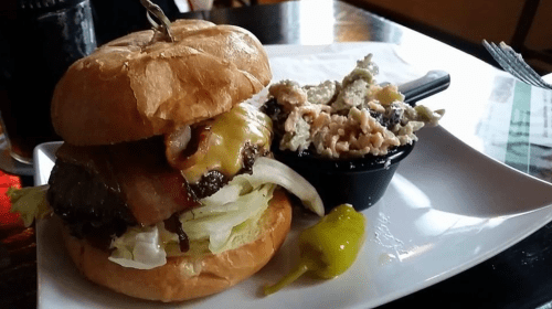 A juicy burger with bacon, cheese, and lettuce, served with a side of creamy pasta salad on a white plate.