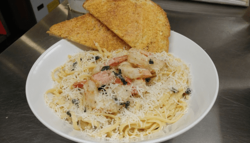 A bowl of fettuccine pasta topped with shrimp, cheese, and herbs, served with two slices of toasted bread.
