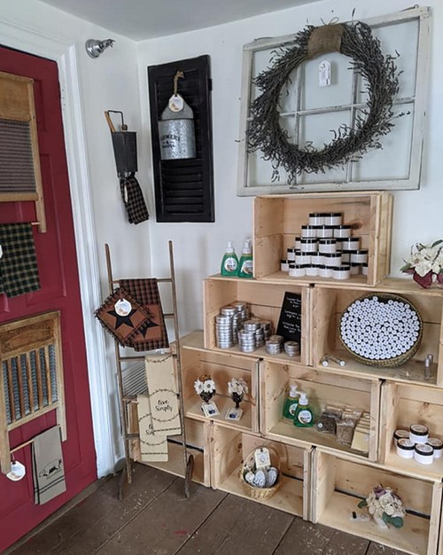 A cozy display of rustic home goods and decor, featuring wooden crates, candles, and a wreath on the wall.