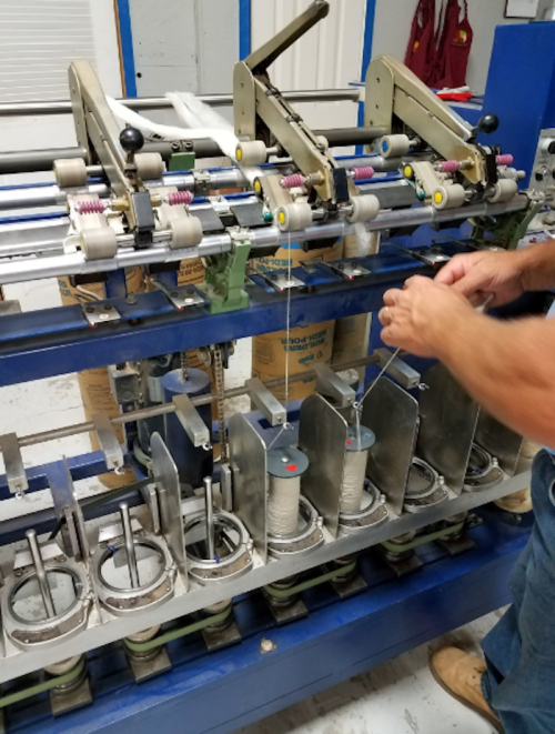 A person operates a machine with spools and metal components, likely for manufacturing or assembly purposes.