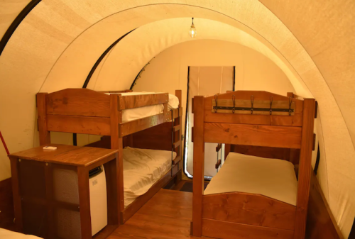 Interior of a cozy tent with two sets of wooden bunk beds and a small table, illuminated by a hanging light.