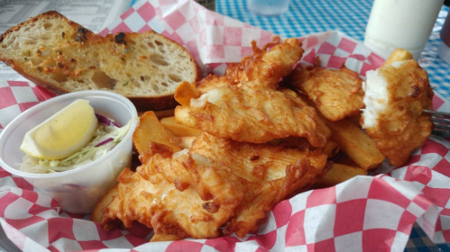 A basket of crispy fried fish fillets, golden fries, coleslaw, a lemon wedge, and a slice of toasted bread.