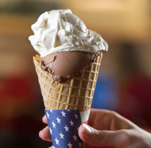 A hand holding a waffle cone filled with chocolate ice cream and topped with whipped cream, wrapped in a star-patterned paper.