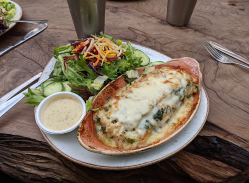 A baked dish with melted cheese, served with a side salad and dressing on a rustic wooden table.