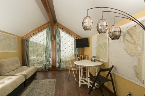 Cozy attic living space with a sofa, dining table, and decorative maps on the walls, featuring large windows with curtains.