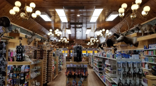 Interior of a rustic store with wooden walls, chandeliers, and shelves filled with various products and mounted animal heads.