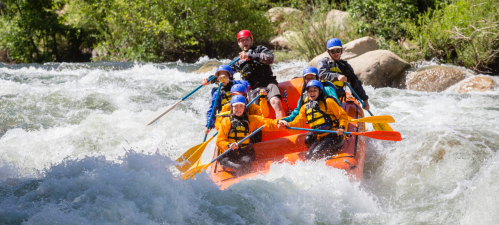 A group of people in a raft navigating a river with rapids, wearing life jackets and helmets, enjoying an adventure.