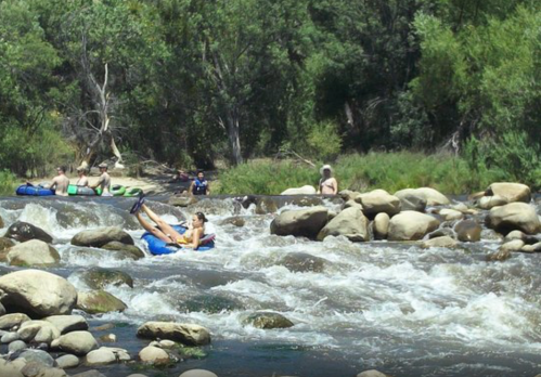 People tubing on a river, surrounded by rocks and greenery, enjoying a sunny day outdoors.
