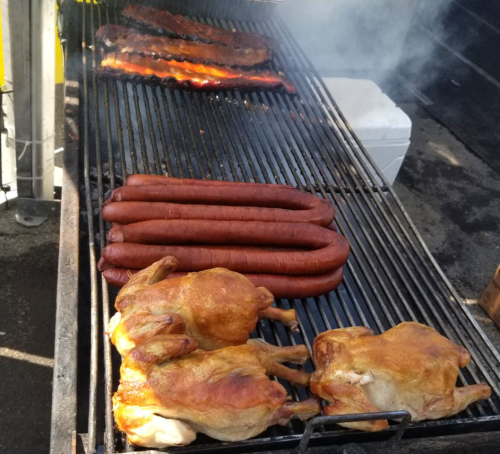 Grilled meats on a barbecue: ribs, sausages, and whole chickens cooking over smoky flames.