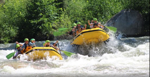 Two yellow rafts navigate through whitewater rapids, with people paddling and wearing helmets in a lush green setting.