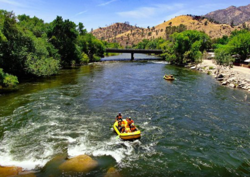 A river with two yellow rafts navigating through calm waters, surrounded by lush greenery and hills in the background.