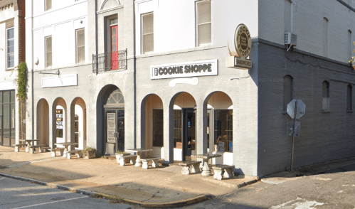 Exterior of The Cookie Shoppe, featuring arched windows and a sign, with outdoor seating on a quiet street.