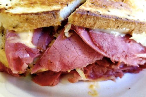 Close-up of a toasted sandwich filled with layers of pink deli meat and melted cheese.