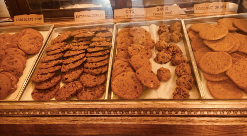 A display of various cookies, including chocolate chip, oatmeal, and coconut drops, in a bakery setting.