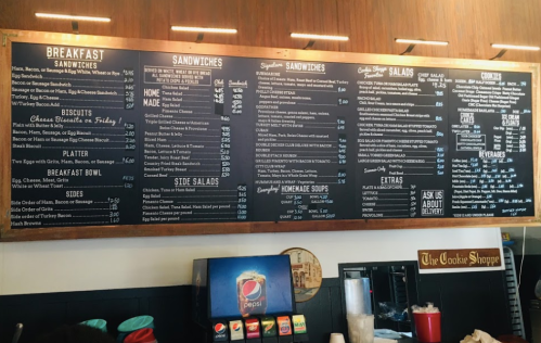 Menu board featuring breakfast items, sandwiches, salads, and desserts with prices listed.