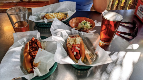 A table with three hot dogs topped differently, a side of coleslaw, and two glasses of beer.