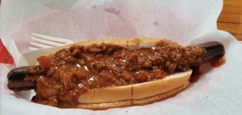 A hot dog topped with chili, served in a bun on a paper-lined tray.