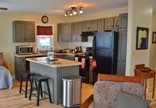 Cozy kitchen with gray cabinets, black appliances, an island, and wooden floors, featuring a seating area.