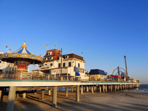 A seaside amusement pier with a carousel, colorful buildings, and a clear blue sky.