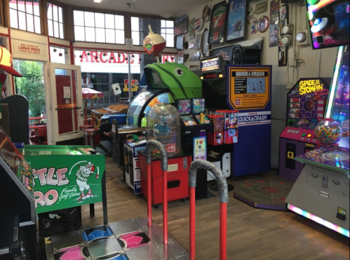 A colorful arcade filled with various games, including pinball machines and a dance game, in a lively setting.