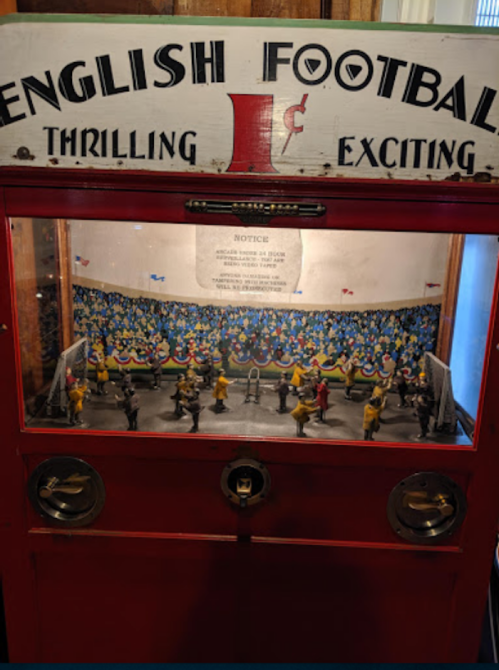 A vintage English football arcade game with colorful players and a crowd backdrop, housed in a red cabinet.