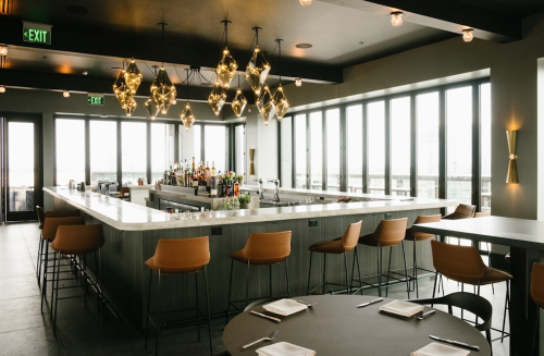 Modern restaurant interior featuring a sleek bar, stylish lighting, and panoramic windows with a view.