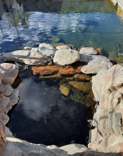 A natural stone pool with clear water reflecting the sky and ripples on the surface.